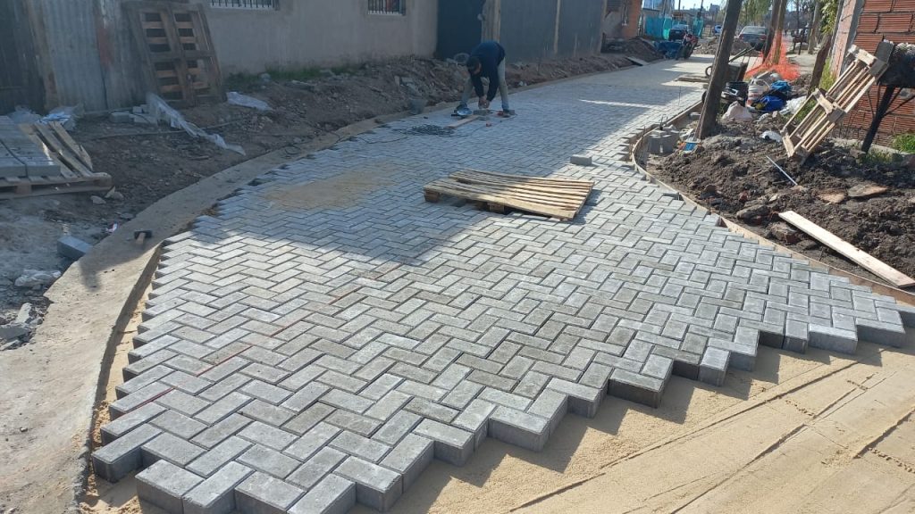 Inicio de obra con adoquines colocados en patrón zigzag sobre base de arena